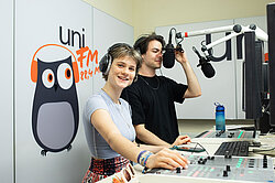 Eine Studentin und ein Student stehen an einem Mischpult mit Mikrofonen im Radiostudio von uniFM 88,4.